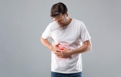 Middle-aged man holding his lightened with red right side, suffering from liver pain, grey studio background, copy space. Sad man having cirrhosis, rubbing his right side. Liver diseases concept