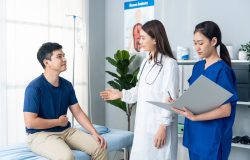 Homen jovem com uma das mãos no abdome enquanto conversa com a médica no consultório sobre o diagnós